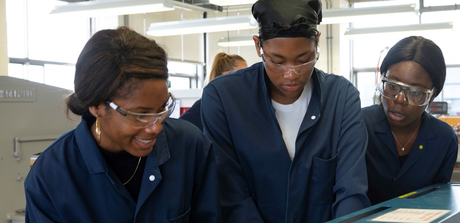 Three students in lab coats looking at a machine